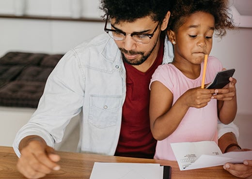 Give Yourself a Pay Raise in 2021—Work at Merit- daughter sitting on dads lap while dad looks at piece of paper and daughter plays with calculator