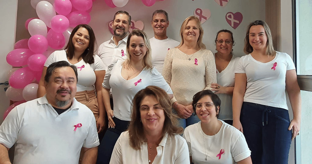 Images of members of the Merit Brazil team wearing pink ribbons on their shirts, posing for a breast cancer awareness photo