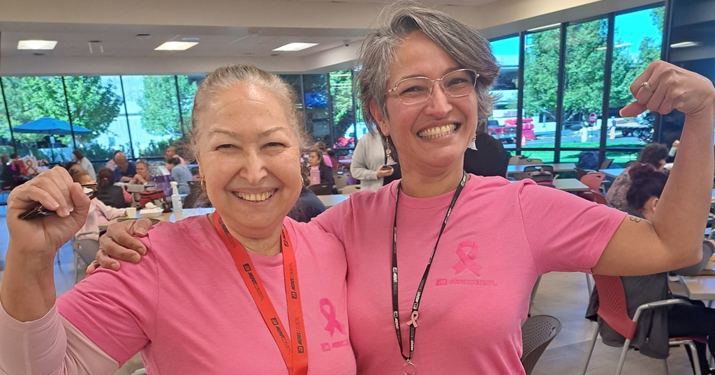 Image of 2 women in pink breast cancer awareness shirts holding up their arms