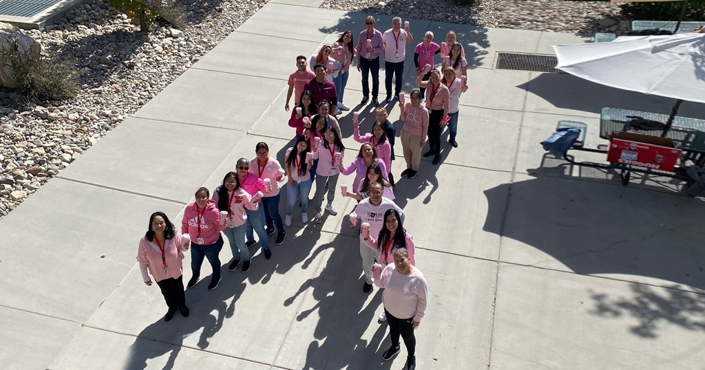 Image of many individuals in pink tops forming the shape of a breast cancer awareness ribbon outdoors