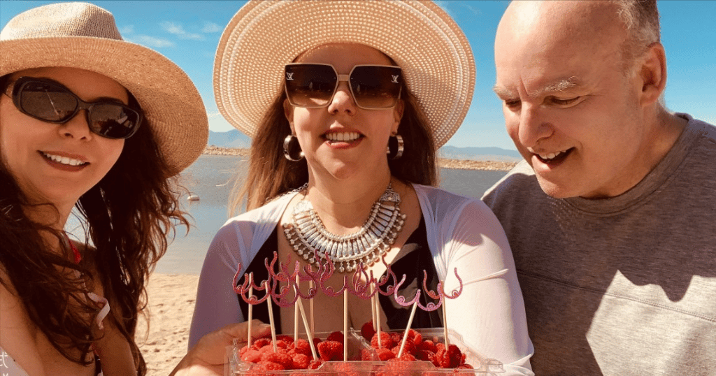 Image of 2 women and a man earing fruit on a beach celebrating the middle woman being breast cancer free