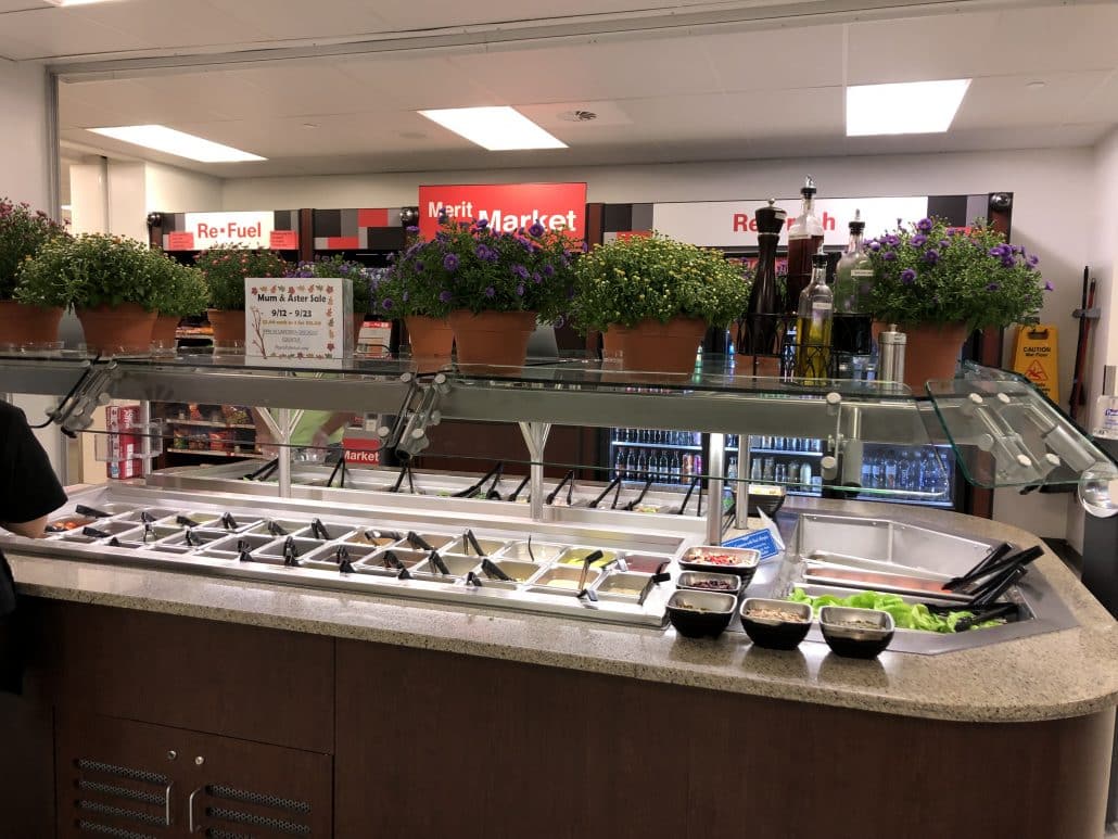 Image shows a salad bar with pots of mums and asters above