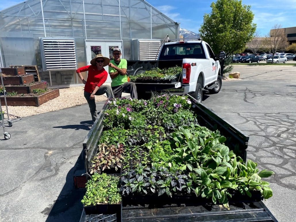 Image shows a truck pulling a trailer with beds of plants ready to be planted at the Merit campus in South Jordan, Utah