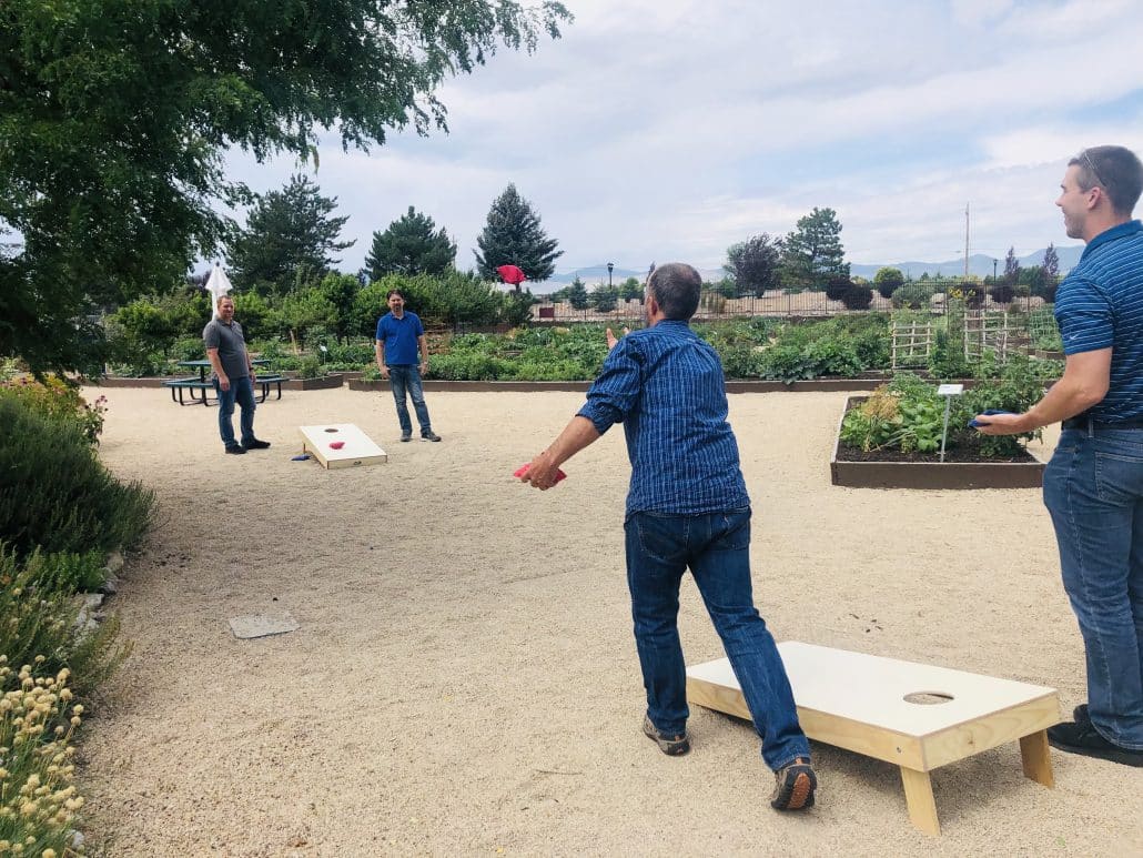 Image shows 4 men playing corn hole at the Merit Gardens in South Jordan, Utah