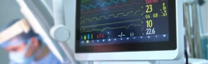Medical monitor showing heart rate and other measurements, with a doctor blurry in the background