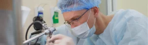 Capped and masked surgeon staring down a medical device