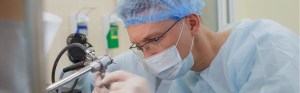Capped and masked surgeon staring down a medical device
