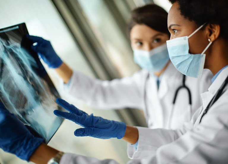 duas médicas mascaradas olhando imagens de raios X