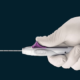 Hand holding a biopsy device laid over a dark background