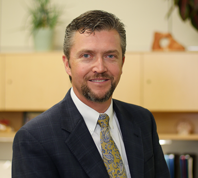 Photo of John Knorpp - Chief Regulatory Affairs Officer - standing in a dark suit & paisley green tie