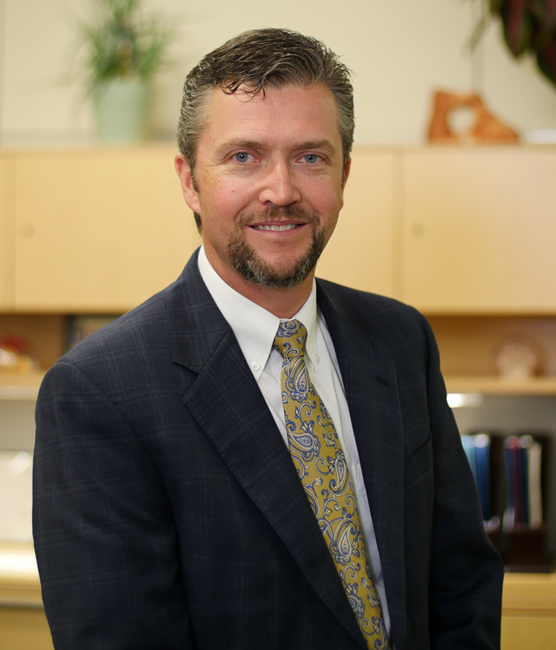 Photo of John Knorpp - Chief Regulatory Affairs Officer - standing in a dark suit & paisley green tie