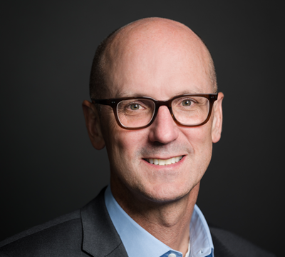 Photo of Joe Wright, Chief Commercial Officer, on a dark background in a blue button down shirt