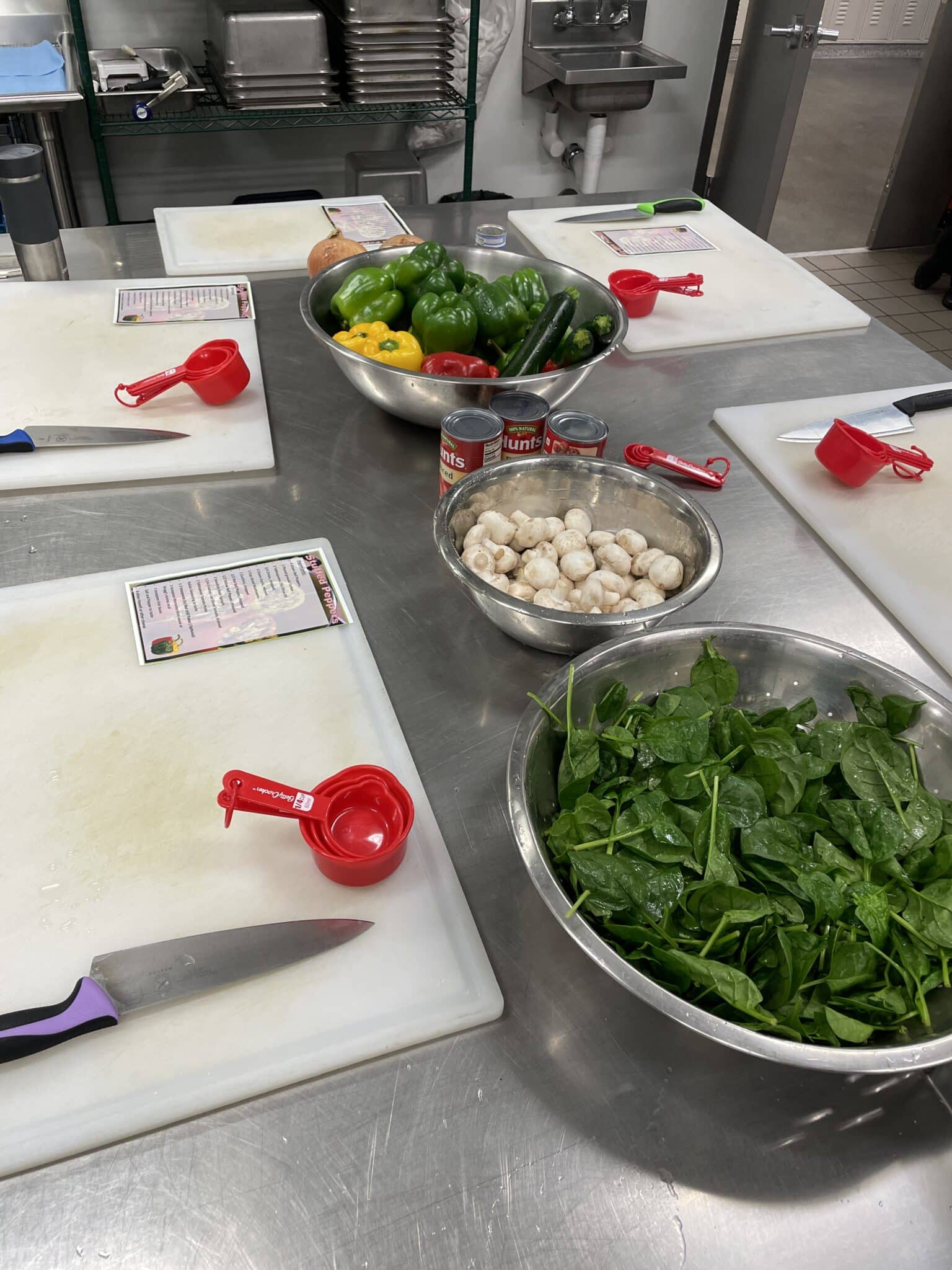Image shows a table with bowls of fresh spinach, mushrooms, bell peppers, ready to be cut up