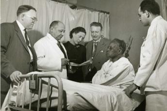 Image of Dr Myra Adele Logan & other doctors next to their patient